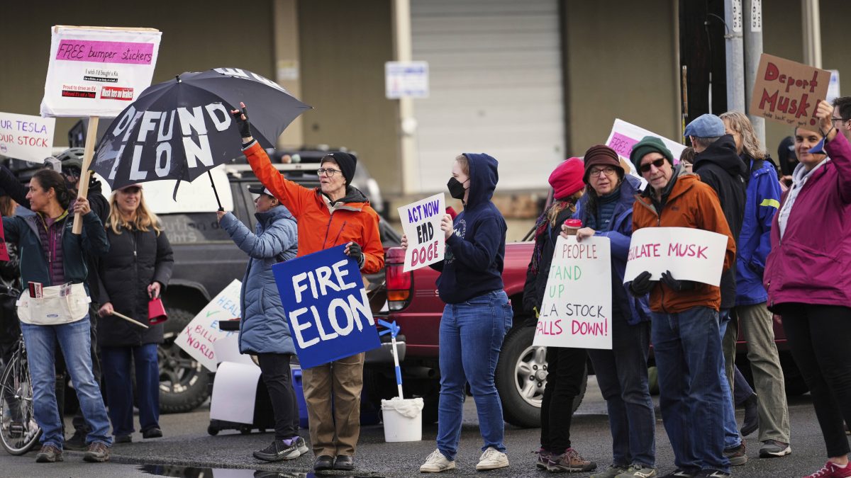 People wave signs to passing cars during a protest against Tesla and Elon Musk outside of a Tesla service center location in Seattle. AP People wave signs to passing cars during a protest against Tesla and Elon Musk outside of a Tesla service center location in Seattle. AP