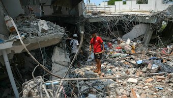 People stand next to a destroyed building as rescuers look through the rubble to find survivors in Mandalay on March 29, 2025, a day after an earthquake struck central Myanmar.Image- AFP
