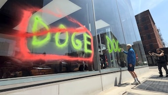A man sprays paint graffiti against Elon Musk's Department of Government Efficiency (Doge) on a Tesla showroom in New York, US, April 22, 2025, in this still image taken from video. Extinction Rebellion NYC via Reuters