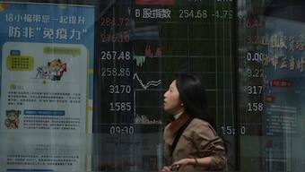 A woman walks by an electronic board displaying shares trading index at a brokerage house, in Beijing, April 7, 2025. AP