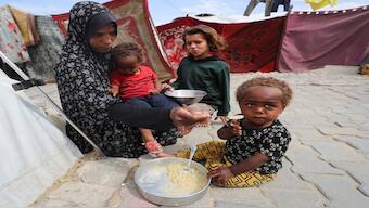 A Palestinian woman feeds her children in front of the tent that shelters them, in Gaza City. Reuters