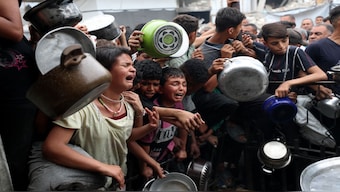 Children react as Palestinians wait to receive food cooked by a charity kitchen, in Beit Lahia, northern Gaza Strip. File Image / Reuters