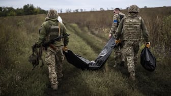 Ukrainian servicemen carry a bag containing the body of a Ukrainian soldier as one of them, right, carries the remains of a body of a Russian soldier in a retaken area near the border with Russia in the Kharkiv region if Ukraine. (Photo: AP)