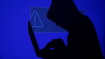 A hooded man holds a laptop computer as blue screen with an exclamation mark is projected on him in this illustration picture taken on May 13, 2017. Representational Image/Reuters