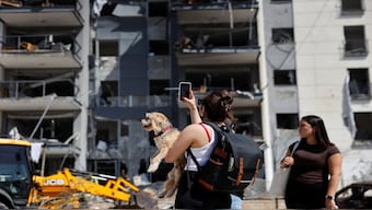 A woman holding a dog takes a photo of a damaged residential building at an impact site following Iran's missile strike on Israel, in Be'er Sheva, Israel. Reuters