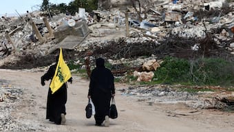 Women walk near destroyed buildings, with one holding the flag of Hezbollah, in the southern Lebanese village of Kfar Kila. File image/ Reuters
