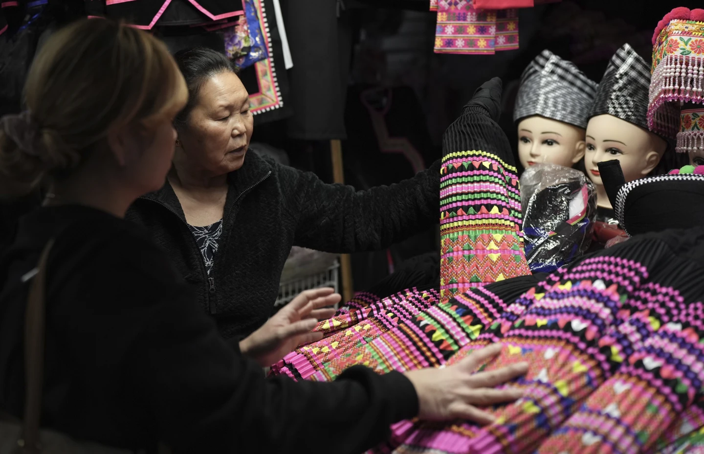 Shoppers look for pleated skirts and other clothing for Hmong New Year for sale at the stall of Elisa Her, left, in the Hmong Village covered market in St. Paul, Minn., on Thursday, Nov. 16, 2023. File Image / AP
