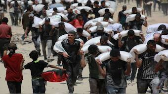 Palestinian walk carrying sacks of flour near Jabalia, in the northern Gaza Strip, on July 27, 2025, after trucks carrying humanitarian aid entered into northern Gaza coming from the Zikim border crossing. AFP