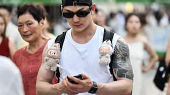 A man walks with two Labubu plush toys hanging from his backpack straps along a pedestrian street on The Bund in Shanghai. The toys are a hit and now fake versions, Lafufu, have flooded the market. AFP