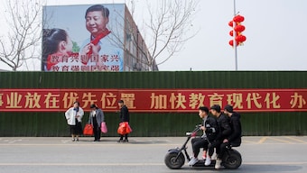 (File) Men ride a scooter past a poster showing Chinese President Xi Jinping on the side of a school building in Henan province, China. Reuters