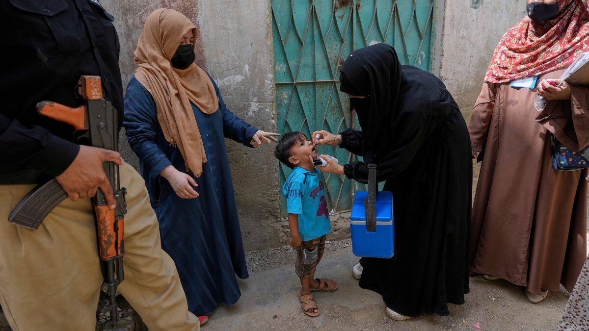 A police officer stands guard while a health worker, centre, administers a polio vaccine to a child in Karachi, Pakistan, April 21, 2025. File Image/AP