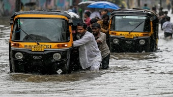 Drivers push their auto-rickshaws through a flooded street during heavy rain showers in Mumbai on Monday. AFP