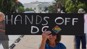 A demonstrator holds a sign during a protest near the White House, as US President Donald Trump announced he is placing the DC Metropolitan Police Department under direct federal control and deploying National Guard troops to Washington, DC. Reuters