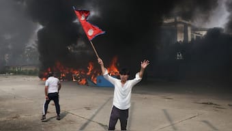 A demonstrator holds Nepal's flag as smoke rises from the Parliament complex in Kathmandu, Nepal, on September 9, 2025, after demonstrators set the building ablaze. (Photo: Adnan Abidi/Reuters)