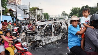 People travel past a car burnt during a protest over lawmakers' pay, escalating on Friday after a police armoured vehicle hit and killed the driver of a ride-hailing motorbike, outside East Jakarta's police headquarters, in Jakarta, Indonesia, August 30, 2025. Reuters