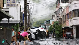 Residents clear mud from their property, while damaged cars are seen in the background, in Hualien on September 24, 2025, following the bursting of a barrier lake. AFP