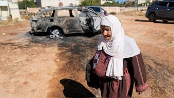 A woman walks past a vehicle that was burnt overnight by Israeli settlers in an attack in June this year. File image/AP
