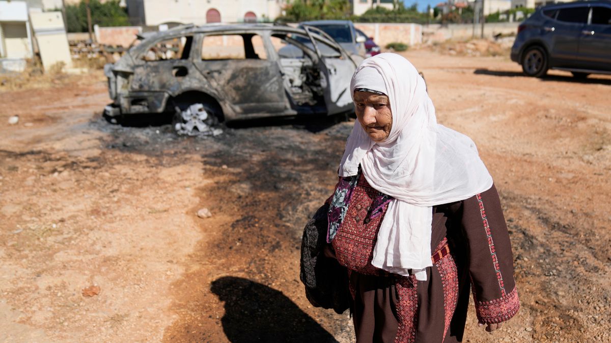 A woman walks past a vehicle that was burnt overnight by Israeli settlers in an attack in June this year. File image/AP A woman walks past a vehicle that was burnt overnight by Israeli settlers in an attack in June this year. File image/AP