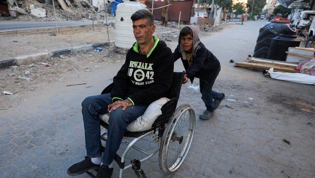 A Palestinian boy pushes a man on a wheelchair on a street next to damaged buildings. Reuters