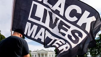 FILE - A man carries a Black Lives Matter flag in Lafayette Square outside the White House on the fourth night of the Republican National Convention, Aug. 27, 2020, in Washington. AP