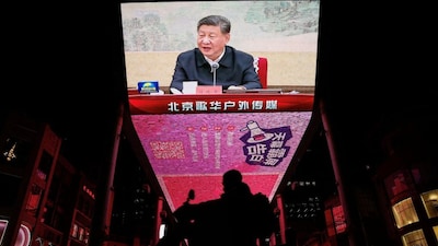 A man rides a scooter past a giant screen showing news footage of Chinese President Xi Jinping attending a Chinese Communist Party politburo meeting, in Beijing, China, December 9, 2024. File Image/Reuters
