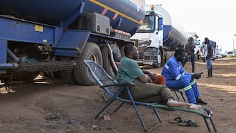 Drivers of Malian tanker trucks sit on chairs while waiting waiting to cross the border between Ivory Coast and Mali in the village of Nigoun, near Tengrela on October 31, 2025. In northern Ivory Coast, truck drivers prepare to head back to neighbouring Mali, aboard their tanker trucks loaded with fuel and anxiety.