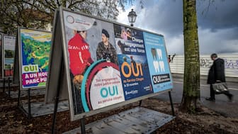 A man walks past voting posters in favor of an initiative for compulsory civic duty for all is seen in a street in Geneva, on November 25, 2025. The Swiss will vote on November 30, 2025 on replacing men's current military service requirement with a compulsory civic duty for all, with backers and opponents alike claiming to be championing women's rights. As part of Switzerland's direct democratic system, voters will also be weighing in on whether to slap new taxes on the super-rich to help finance the country's effort against climate change. (Photo by Fabrice COFFRINI / AFP)