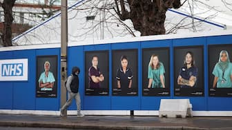 A person walks past images of National Health Service (NHS) workers displayed on hoardings outside a temporary field hospital at St George's Hospital in London, UK, January 8, 2022. File Image/Reuters