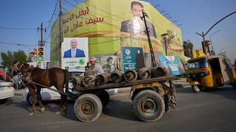 A laborer riding a horse cart carrying cooking gas cylinders, passes elections posters in Baghdad, Iraq (Image: AP)