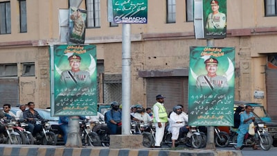 A police officer stands in front of the traffic, next to posters of the Chief of Army Staff of Pakistan Asim Munir, in Karachi. File image/Reuters