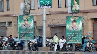 A police officer stands in front of the traffic, next to posters of the Chief of Army Staff of Pakistan Asim Munir, in Karachi. File image/Reuters
