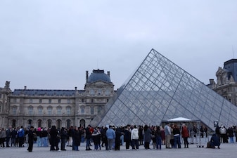 People stand near the glass Pyramid of the Louvre Museum which remains closed in Paris, France. Reuters