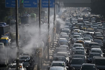 Commuters drive past as anti-smog sprinklers on lamp posts spray water to curb air pollution in New Delhi (AFP)