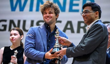 Norway's chess grandmaster Magnus Carlsen (C) receives the winner trophy from Indian chess grandmaster Viswanathan Anand (R) during the Tata Steel Chess India tournament in Kolkata on November 17, 2024. AFP