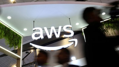 People walk past the logo of Amazon Web Services (AWS) at its exhibitor stall at the India Mobile Congress 2025 at Yashobhoomi, a convention and expo center in New Delhi, October 8, 2025. File Photo/Reuters