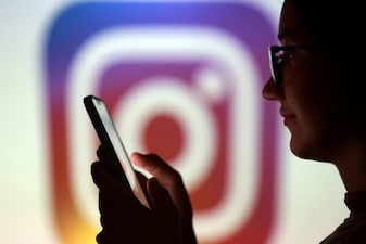 A teenager poses for a photo while holding a smartphone in front of a Instagram logo. REUTERS/Dado Ruvic/Illustration