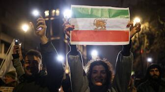 A woman holds up a paper print of the "Lion and Sun" pre-Iranian Revolution national flag as demonstrators walk toward the Iranian embassy during a rally in London, Britain. Reuters