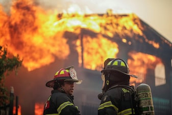 Firefighters stand in front of a burning building in the aftermath of a forest fire in the Biobio region where multiple wildfires prompted emergency evacuations in Concepcion. Reuters