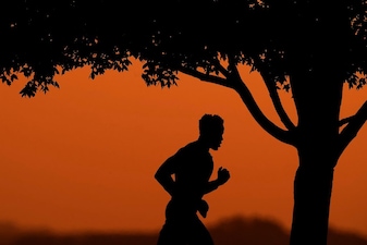 A man is silhouetted against the sky at sunset as he jogs in a park at the close of a hot summer day in Kansas City. File image/AP