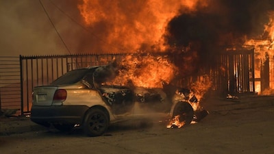 A vehicle and a house are engulfed in flames during a wildfire in Concepcion, Chile, on January 18, 2026.- AFP