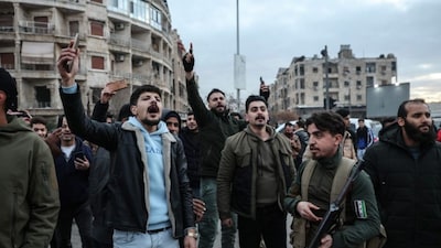 Residents react as a bus carrying men who state media reported to be Kurdish fighters prepares to leave Aleppo's Kurdish-majority Sheikh Maqsud neighbourhood accompanied by security forces on January 10, 2026.
