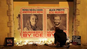 A person kneels near posters with images of Renee Nicole Good and Alex Pretti, after they were fatally shot in two separate incidents by federal immigration agents, following a vigil in Minneapolis, Minnesota. Reuters