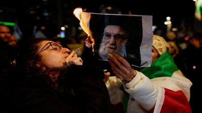A woman lights a cigarette with fire from a burning picture of Iran's Supreme Leader Ayatollah Ali Khamenei, as Israelis rally in support of the nationwide protests happening in Iran, in Holon, Israel. Reuters