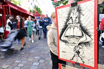 Pedestrians walk past a caricature portrait at the Place du Tertre on the hill of Montmartre, northern Paris. File image/AFP