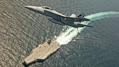 An F/A-18F Super Hornet jet flies over the USS Gerald R. Ford as the U.S. Navy aircraft carrier tests its EMALS magnetic launching system.  File- Reuters
