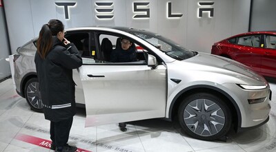 A woman opens the door for a Tesla Model YL electric vehicle as a customer looks inside at a showroom in Beijing on February 3, 2026. Image Credit: AFP