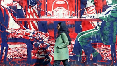An Iranian woman walk past anti-US mural depicting Iran and US negotiation table, painted on the outer walls of the former US embassy, in Tehran. AFP