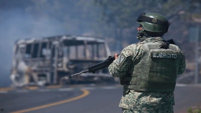 A soldier stands guard by a charred vehicle after it was set on fire in Cointzio, Michoacán state, Mexico, Sunday, after the death of the leader of the Jalisco New Generation Cartel, Nemesio Rubén Oseguera Cervantes, known as "El Mencho." AP