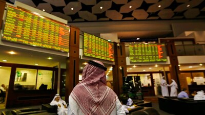 An investor looks up at screens displaying stock information at the Dubai Financial Market. Reuters