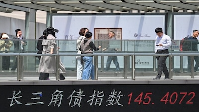 People walk across a bridge with a board showing the bond index in Yangtze River Delta region at the financial district in Shanghai. (File/AFP)